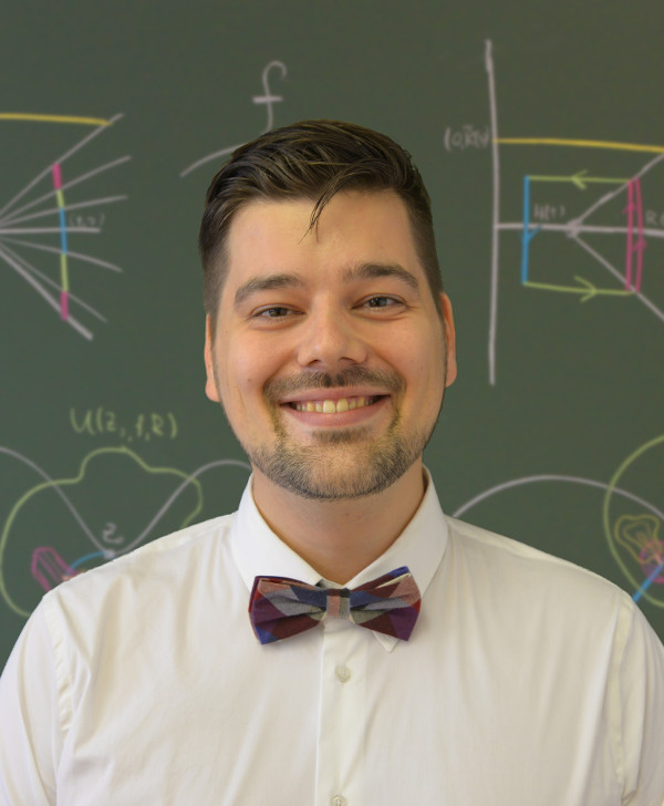 Rami Luisto smiling in front of a blackboard with some colorful pictures.